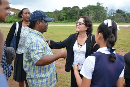 First Lady, Mrs. Sandra Granger greets Mahdia businessman Mr. Roger Hinds as student, Ms. Lucianna Thomas waits to drape a beaded flag-colour necklace around her neck. Mr. Hinds explained that the necklace is a handmade gift from 65-year-old Ms. Marlyn Gouveia.
