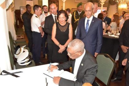 President David Granger signs the Book of Condolences, which was opened at the Reception in observance of France's National Day, for the victims of the terrorist attack in Nice. First Lady, Mrs. Sandra Granger and France's Ambassador to Guyana, Mr. Michael Prom look on.