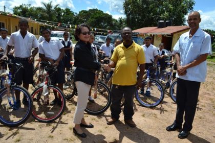 First Lady, Mrs. Sandra Granger and Mahdia businessman, Mr. Roger Hinds shake hands as Regional Executive Officer, Mr. Rafel Downes and some of the recipients of spanking new bikes look on. 