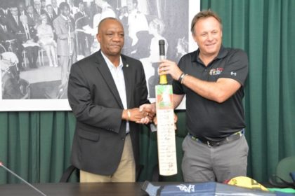Minister of State, Mr. Joseph Harmon receives a bat bearing the autographs of the players in the Guyana Amazon Warriors team from Mr. Pete Russell, Chief Operations Officer, Caribbean Premier League. 