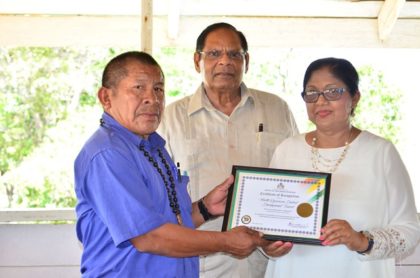 NRDDB Vice Chair Michael Williams receives the OPM Certificate of Recognition from Mrs Sita Nagamootoo while Prime Minister Moses Nagamootoo looks on.
