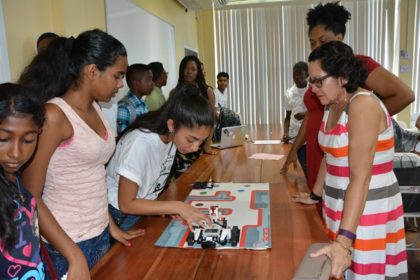 First Lady, Mrs. Sandra Granger pays keen attention as Ms. Kavya Sony, one of the trainers at the workshop held at the Friendship Primary School, makes a small adjustment to her group’s robot. Ms. Karen Abrams is pictured behind the First Lady.