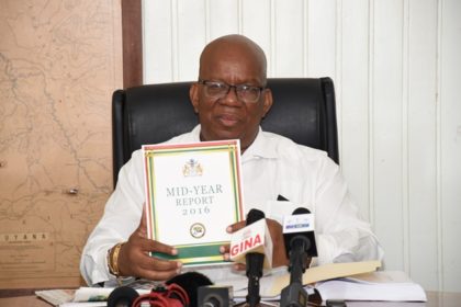 Minister of Finance, Winston Jordan displays a copy of the Midyear report at the Ministry of Finance