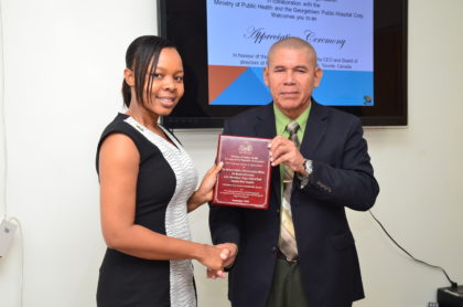 Minister of Public Health Dr. George Norton presents a plaque to President of Guyana Help The Kids (GHTK) Guyana Chapter, Dr. Winsome Scott