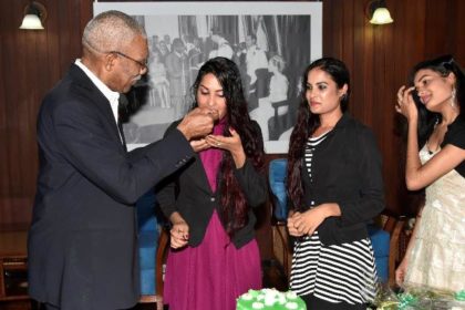 President David Granger gives Ms. Radha Mansaram a piece of her birthday cake as her sisters look on.