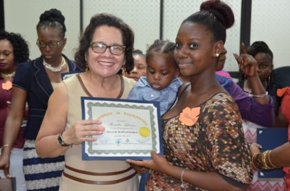 First Lady, Mrs. Sandra Granger helps Ms. Shemika Solomon to display her certificate as she holds her son, at the graduation ceremony of the Self Reliance and Success in Business Workshop for women 